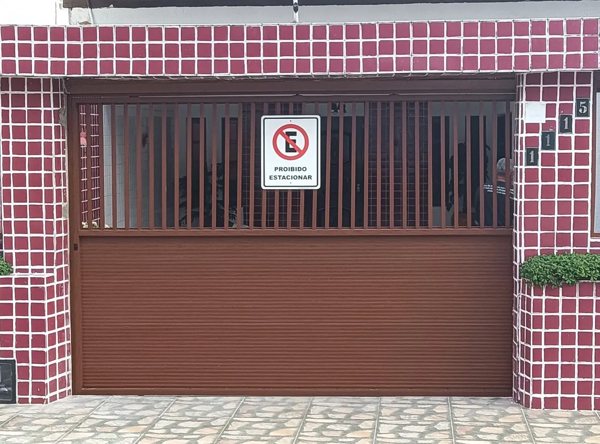 Portão de alumínio marrom com palhetas superiores e placa de proibido estacionar